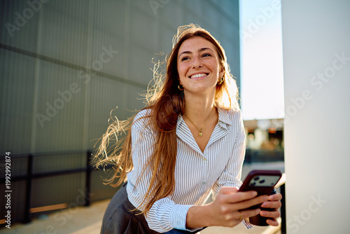 Tableau sur toile Young woman with freckles and long red hair smiling widely, leaning outdoors whi