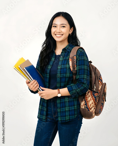 Cheerful  Indonesian college student posing with books and batik motif backpack isolated on white background.