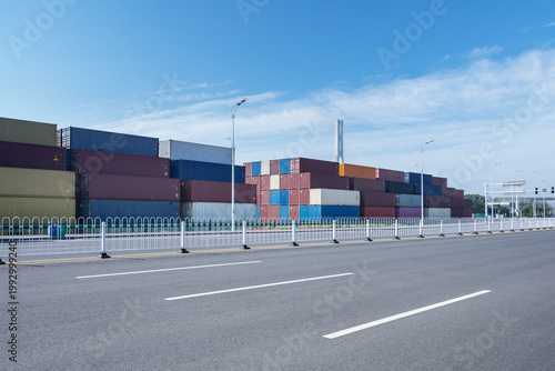Colorful Shipping Containers Stacked Behind Road Background Under Clear Blue Sky
