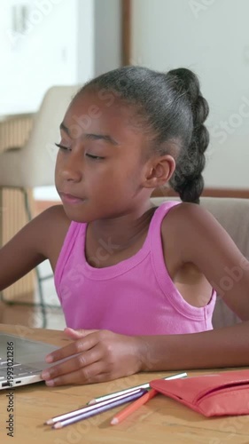 Vertical video: Glancing left, child in pink top using laptop pad at table, learning with pencils