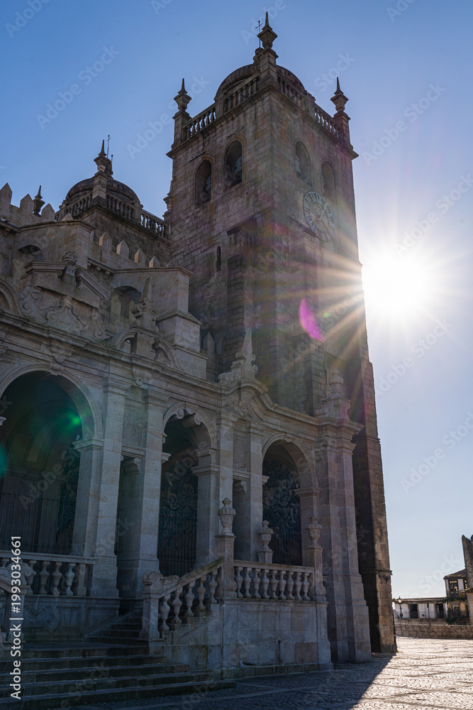 Obraz premium Facade of Porto Cathedral Se in Porto Portugal with arches stone columns and clock tower. Historic religious landmark with medieval architecture under clear blue sky.