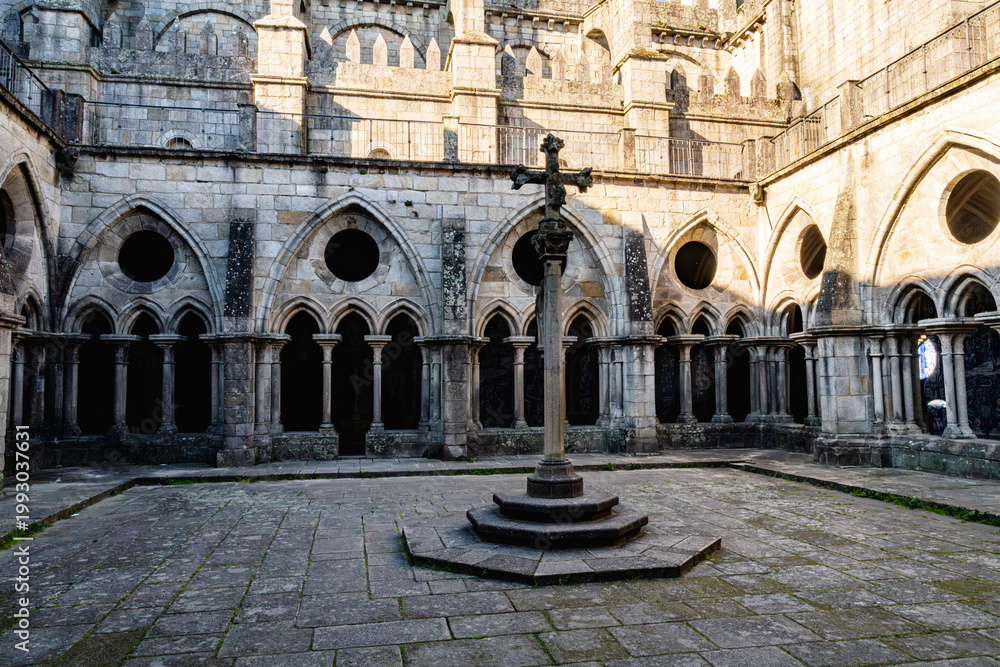 Fototapeta premium Historic cloister courtyard of Porto Cathedral with gothic arches and stone columns surrounding central cross monument. Ancient religious architecture in Portugal with peaceful atmosphere.