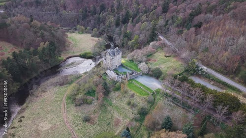 A majestic historic castle standing on a rocky crag above the River Tweed, surrounded by the scenic landscape of the Scottish Borders in Peebles