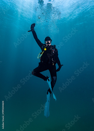 A scuba diver having fun underwater, doing a funny dance pose on the safety stop in mid-water