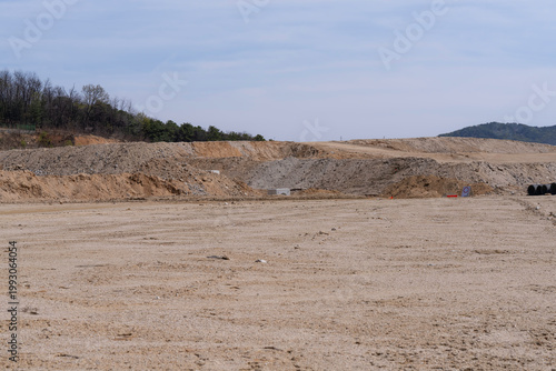 Wide construction site with excavated soil, leveled ground, and distant hills under clear sky, showing early stage land preparation for infrastructure development project.