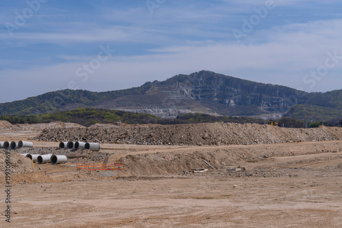 Wide construction site with excavated soil, leveled ground, and distant hills under clear sky, showing early stage land preparation for infrastructure development project.