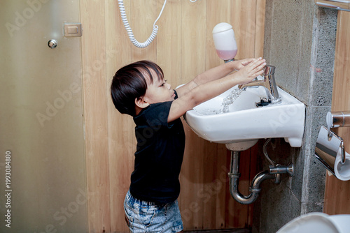 Asian Boy Washing Hands Carefully At White Bathroom Sink