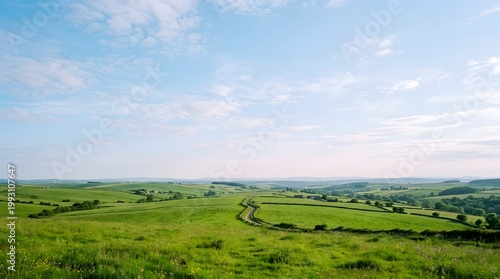 Vast green rolling hills stretch under a bright expansive sky, showcasing peaceful summer countryside scenery with gentle sunlight illuminating the distant landscape