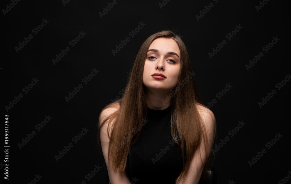 Fototapeta premium Young woman with long brown hair posing for an elegant portrait, looking directly at the camera with a confident expression