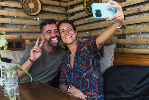 Smiling couple enjoying vacation while taking a selfie with a smartphone in bamboo decor
