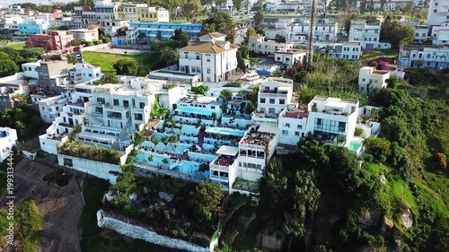 Cinematic drone shot of the iconic Cafe Hafa in Tangier, Morocco, featuring its famous terraces overlooking the Mediterranean Sea and the Spanish coast.