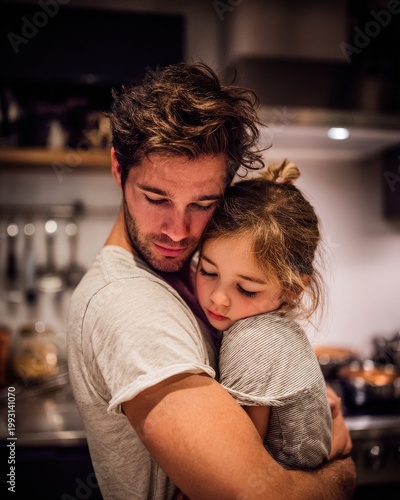 Father holds his daughter in his arms while they share a quiet moment in the kitchen during the evening