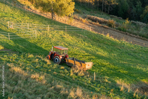 An old tractor with a trailer sits in the middle of a meadow.