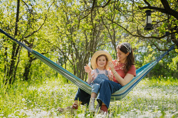 Happy Mother's Day concept with beautiful woman and little daughter embracing in garden hammock