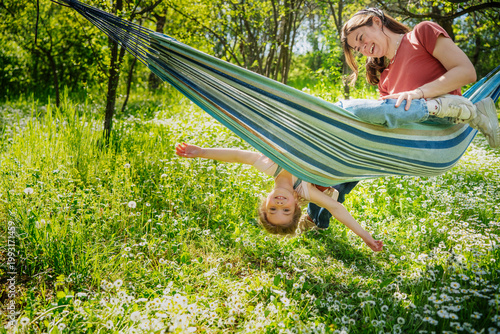 Fotografie Playful little girl hanging upside down from hammock while playing with her moth