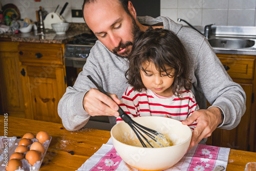father daughter baking together at home in the kitchen making dough, concept of fatherhood and bonding with children, cooking together with complicity