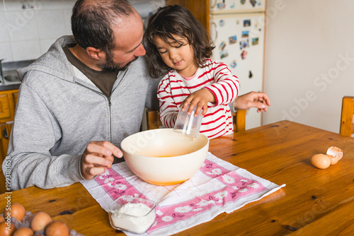 father daughter baking together at home in the kitchen making dough, concept of fatherhood and bonding with children, cooking together with complicity