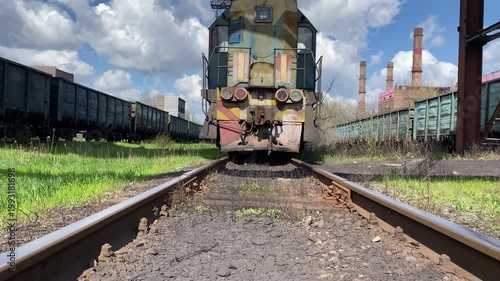 Old diesel locomotive standing on railway tracks at a station against blue sky. Camera moves upward from low angle. Concept of transportation, industry, logistics and rail infrastructure. 4K video.