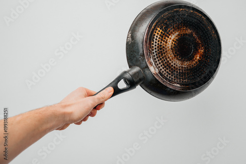 Male Hand Holding Old Dirty Frying Pan with Burnt Bottom Against Grey Background