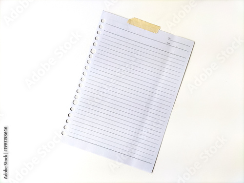 A single sheet of lined paper is attached to a surface using a piece of beige tape at the top