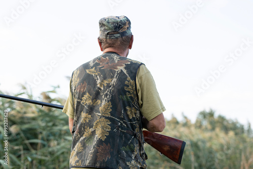 A hunter with a gun in camouflage clothing. A senior man with a gun, medium shot, searching for game.
