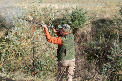 An adult hunter hunts in the autumn countryside. He fires a shotgun.