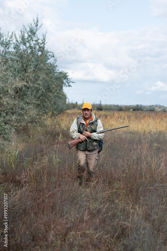 A hunter with a gun in camouflage clothing. A senior man with a gun, medium shot, searching for game.