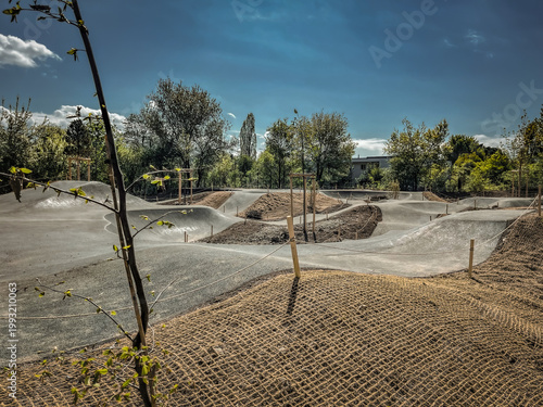 sunny day at a dirt bike track with ramps and barriers, surrounded by trees and blue sky