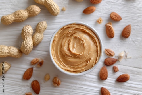 A Bowl of Creamy Peanut Butter Surrounded by Peanuts and Almonds on a White Wooden Table Top View of Delicious Nut Butter Spread Ready for Breakfast or Snacking
