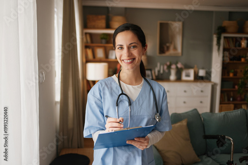 Foto A home health nurse stands in a living room smiling while holding a clipboard