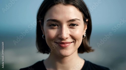 A young woman smiling and expressing peaceful emotions outdoors.