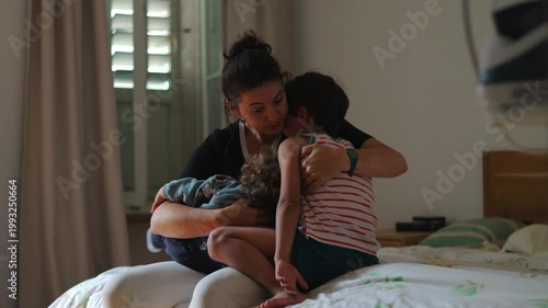 Mother sitting on bed embracing two children close together offering comfort during difficult moment showing warmth care emotional support and quiet resilience in family life
