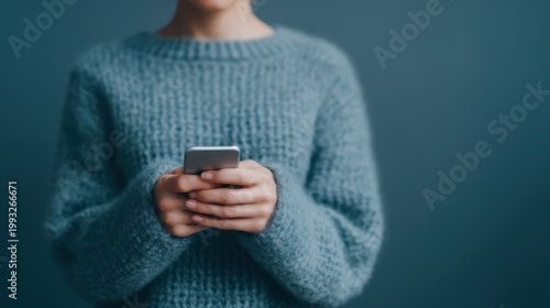 Password security, A person in a blue knitted sweater is using a smartphone against a blue background, focusing on their hands and the device.
