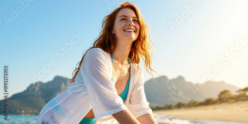 Slender red-haired woman wearing white shirt over turquoise bikini, posing at beach with mountains in soft focus in the background, sunlight catching her hair.
