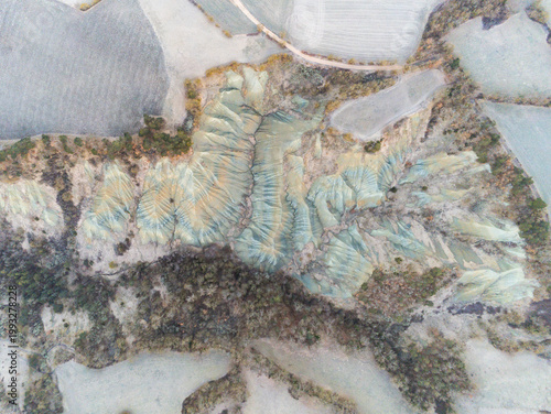 Aerial view of the Ravin de Corboeuf showing its unique multi-colored clay formations and deep ridges surrounded by dense forest and fields in Rosieres, Auvergne-Rhone-Alpes, France.