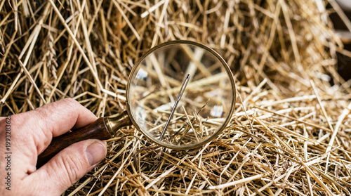 Hand using magnifying glass to find the needle in a haystack