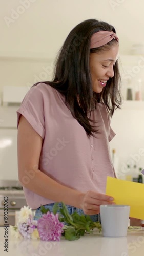 Vertical video: Reading mom in pink top at counter, holding yellow card, as child entering sharing
