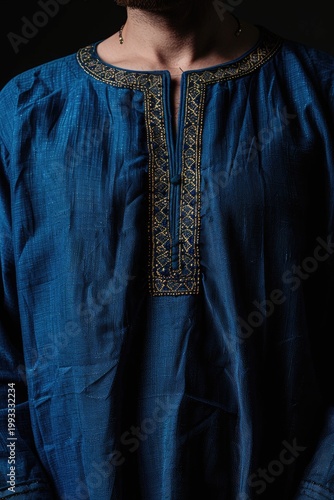 Man in adorned tunic on dark background, showing attire details for fashion ads