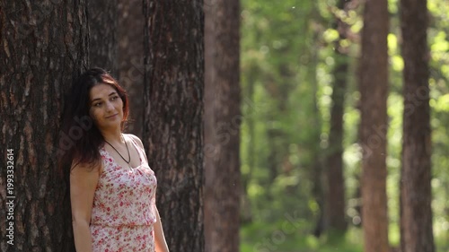 A young woman in a forest. A pretty woman rests in a forest, leaning against a pine tree trunk.