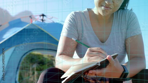 Woman travel journaling at campsite, camera moving from hands to face, grid overlay showing drone