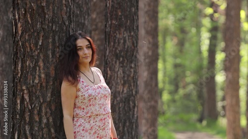 A young woman in a forest. A pretty woman rests in a forest, leaning against a pine tree trunk.