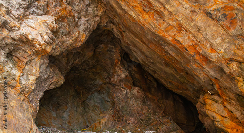 Interior of a rock cave featuring reddish-brown stratified geological formations and textured stone structures