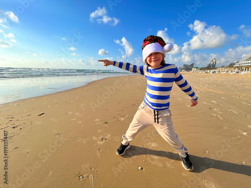 Christmas on the island! A boy in a Santa Claus hat on the beach by the sea. Winter holidays, family vacation