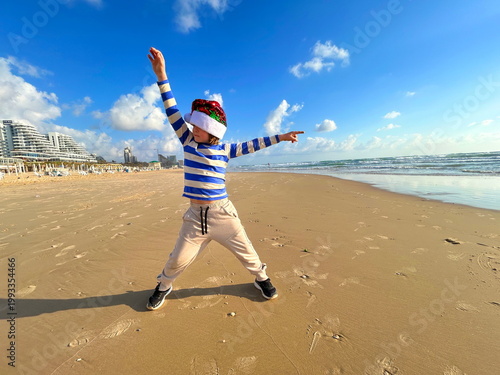 Christmas on the island! A boy in a Santa Claus hat on the beach by the sea. Winter holidays, family vacation