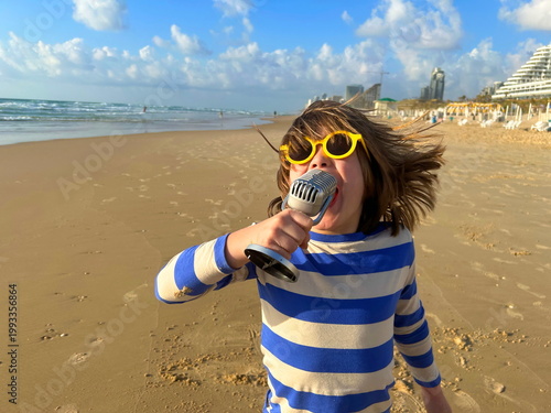 A child boy with a microphone. Rock star. A boy in sunglasses on the beach - travel blogger. Family resort Karaoke