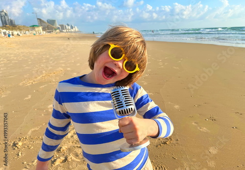 A child boy with a microphone. Rock star. A boy in sunglasses on the beach - travel blogger. Family resort Karaoke
