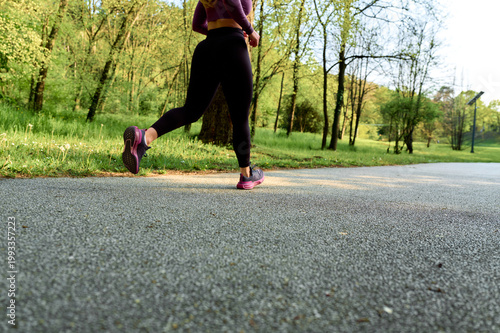 Tablou pe pânză Woman running outdoors on an asphalt path in a public park, focusing on health,