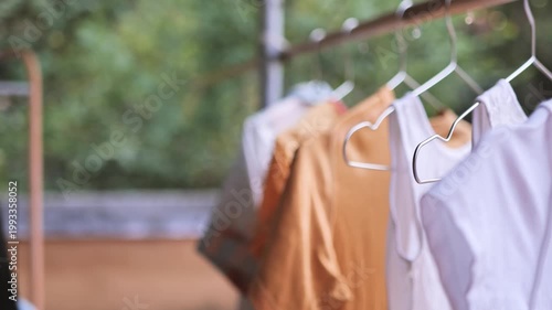 Close-up of clothes hanging on metal hangers while a woman arranges laundry on an outdoor drying rack. The image reflects household chores, clean clothing, domestic routine, fresh air drying, and ever