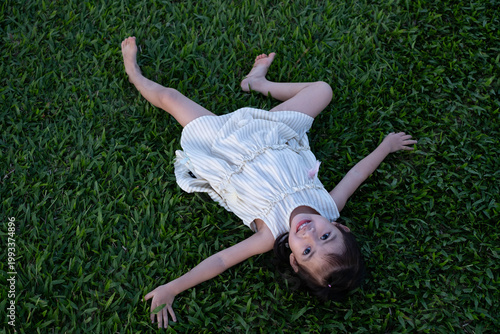 Foto Happy little girl lying on green grass and smiling at camera in a park
