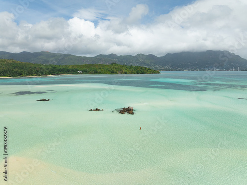 Aerial view of Sainte Anne Marine National Park featuring turquoise waters, white sandbars, and a person standing in the shallows in Victoria, Mont Fleuri, Seychelles.